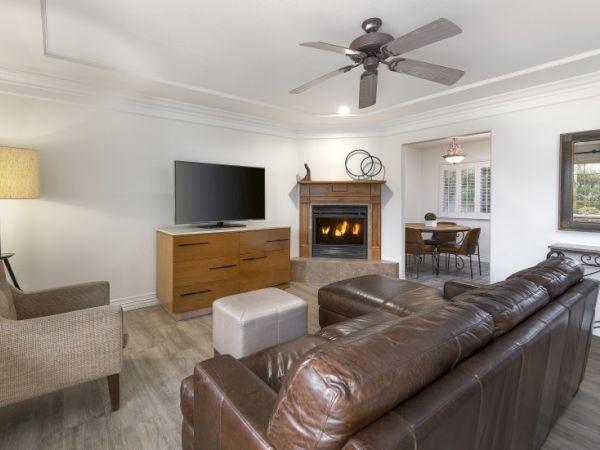 Cozy living room with a leather sofa, fireplace, flat-screen TV, wooden dresser, a ceiling fan, a floor lamp, and a nearby dining area, bright and modern.