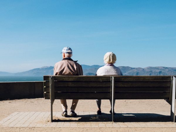 Two people sitting on a bench facing the water and distant mountains.
