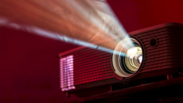 A red projector beams a bright light onto a screen, casting a focused image in a dark, moody room.