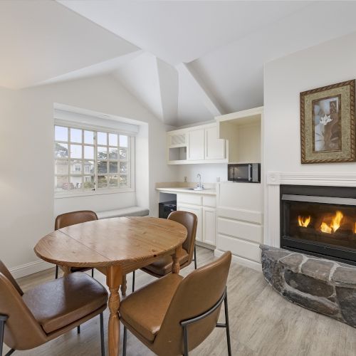 A cozy dining nook with a round wooden table, four brown chairs, and a gas fireplace in a bright, white-kitchen open-plan space.